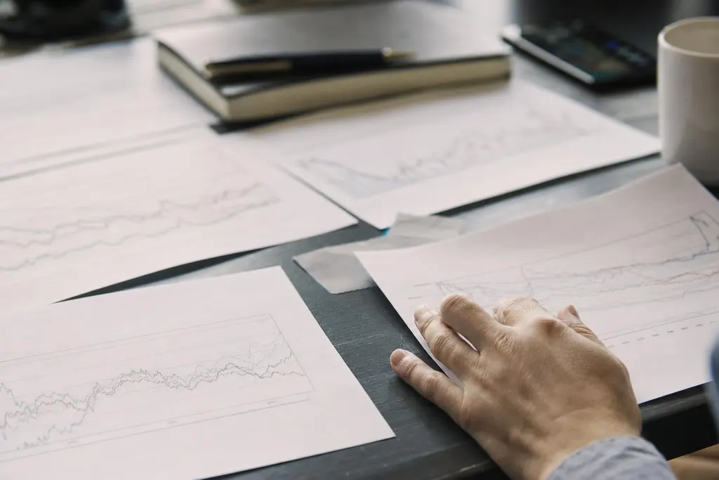 Printed performance charts spread across a desk beside a laptop
